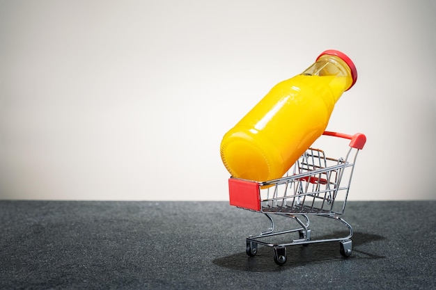 Bottle with orange juice in shopping cart on tile surface with copy space concept supply orange juice vitamins