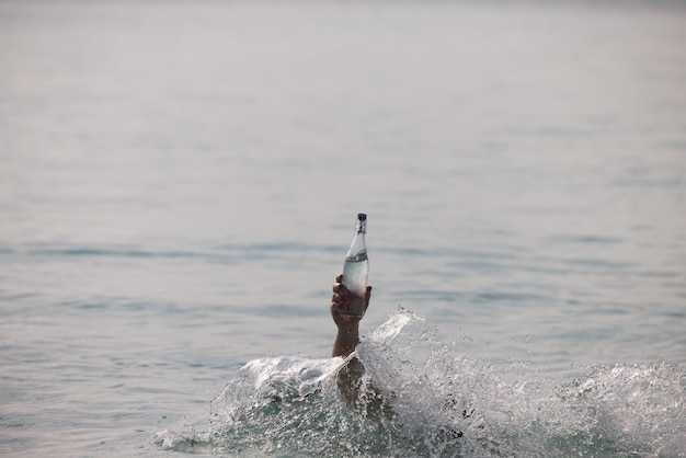 Bottle with pure water in the hand in ocean and splash around it