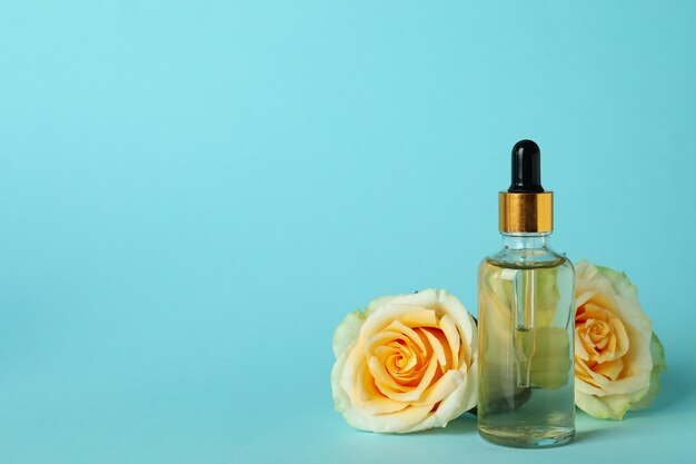 Bottle with rose essential oil and roses on blue background