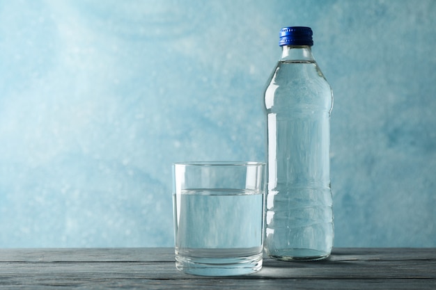 Bottle with water and glass on wooden table, space for text