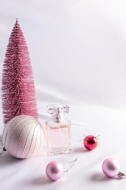 A bottle of women's perfume of a delicate aroma against the a pink Christmas tree and balls the concept of advertising a fragrance gift