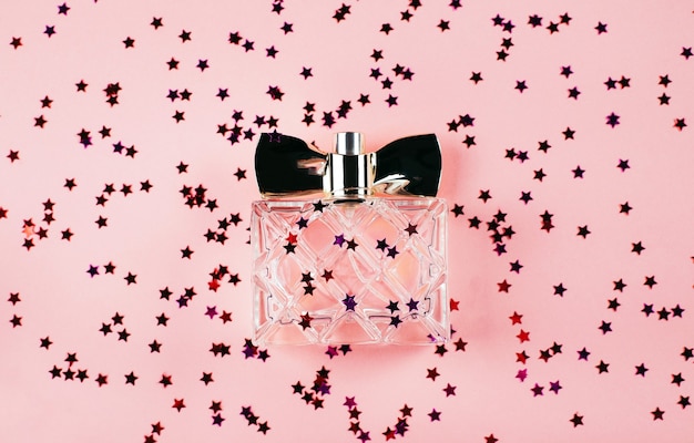 A bottle of women's perfume on a festive pink background with multi-colored sparkles and confetti. view from above. holiday concept february 14 or march 8.