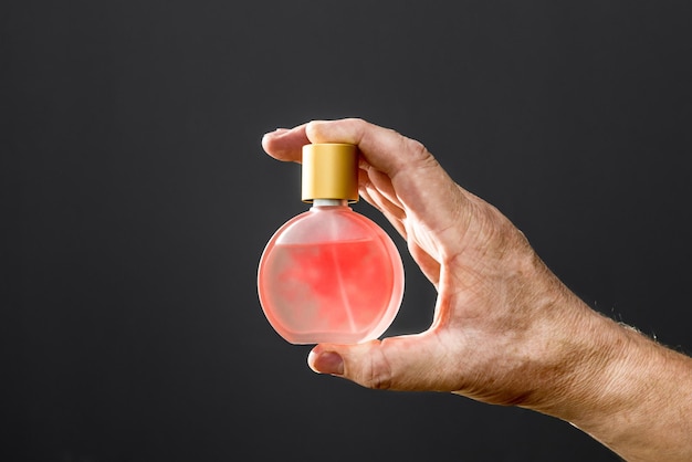 A bottle of women's perfume in a man's hand on a black background