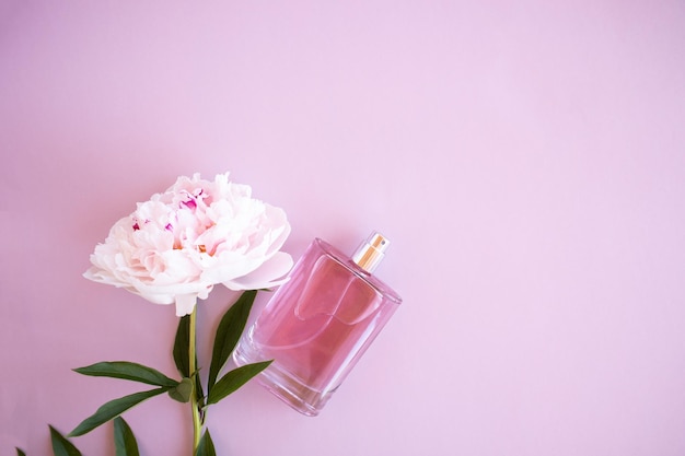 Una bottiglia di profumo da donna su sfondo rosa con una vista dall'alto di peonia una copia dello spazio il concetto di profumeria e bellezza