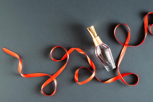 A bottle of women's perfume and a red ribbon on a black background. Layout. Gift for Christmas, Valentine's Day, Women's Day, Mother's Day. Horizontal photo. Place for your text. Advertising flyer.