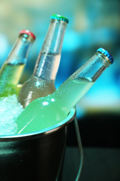 Напитки в бутылках в ведре со льдом на столе на ярком фоне