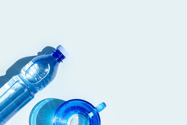 Foto acqua in bottiglia una bottiglia di acqua minerale e un bicchiere d'acqua con ombre dure su sfondo blu disposizione piatta vista dall'alto copia spazio