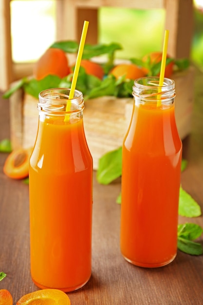 Bottles of apricot juice and fresh fruits on table close up