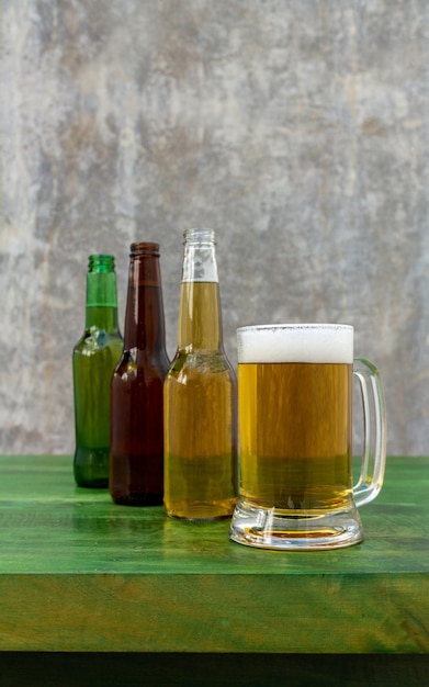 Bottles of beer on a wooden table with a gray background and a beer mug with foam served