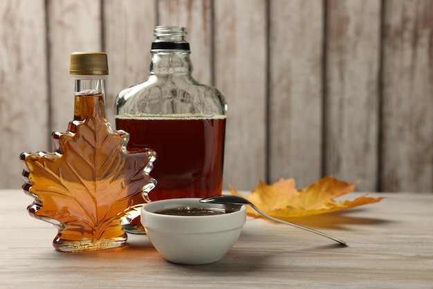 Bottles and bowl of tasty maple syrup on wooden table space for text