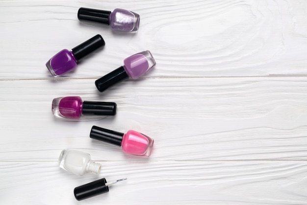 Bottles of colorful nail polish on white wooden background top view with space for text