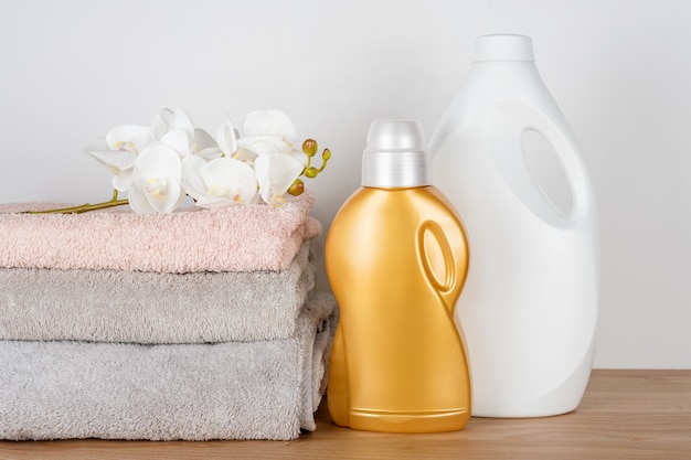Bottles of detergent and fabric softener with clean towels and orchid flowers on wooden table. Containers of cleaning products. Liquid detergent and conditioner. Laundry day, cleaning concept.