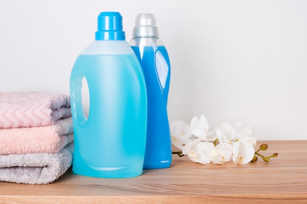 Bottles of detergent and fabric softener with clean towels and orchid flowers on wooden table