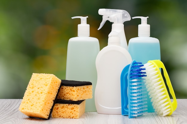 Bottles of dishwashing liquid, brushes and sponges on on blurred background.