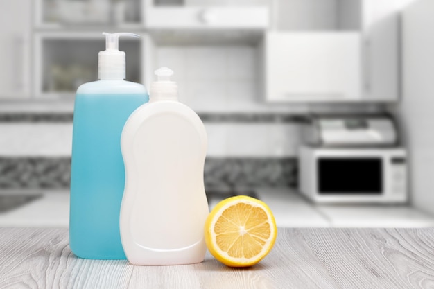 Bottles of dishwashing liquid and lemon on gray background