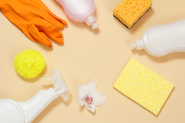 Bottles of dishwashing liquid rubber gloves and sponges on a beige background