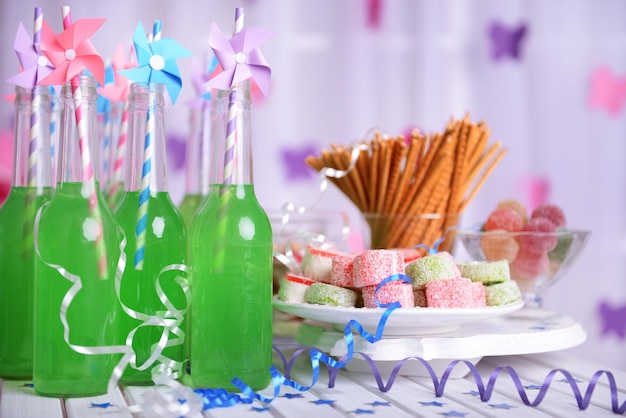 Bottles of drink with straw and sweets on decorative background