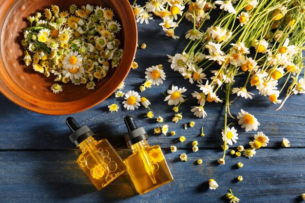 Bottles of essential oil and chamomile flowers on wooden table