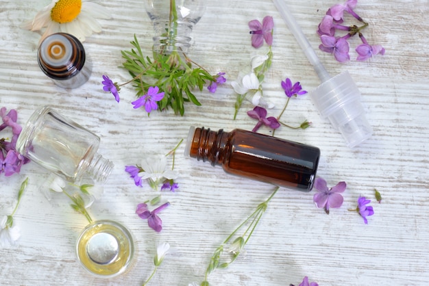 Bottles of essential oil and colorful petals of flowers on white table