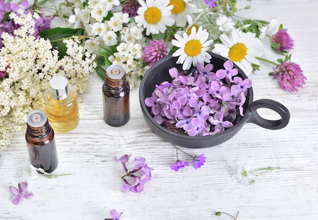 Bottles of essential oil and colorful petals of freshness flowers on white table