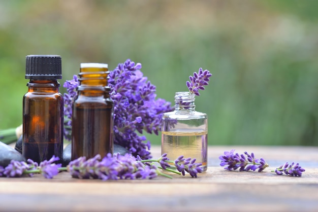 Bottles of essential oil among lavender flower arranged on a wooden table in garden