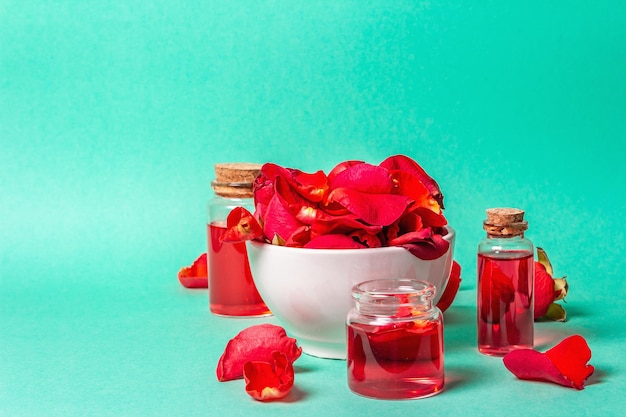 Bottiglie di olio essenziale e petali di rose su sfondo turchese opaco. spa naturale o concetto di cucina, copia spazio