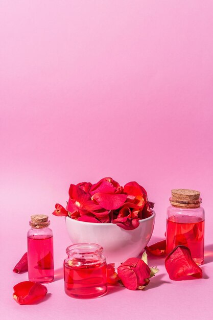 Bottles of essential oil and roses petals on pink background. Trendy hard light, dark shadow, place for text