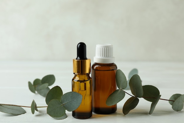 Bottles of eucalyptus oil and twigs on white wooden background