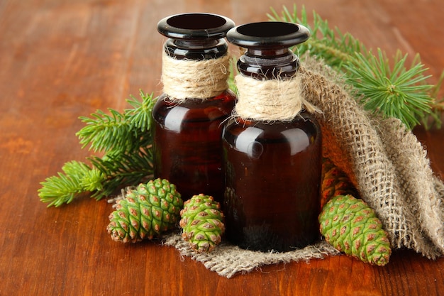 Bottles of fir tree oil and green cones on wooden background