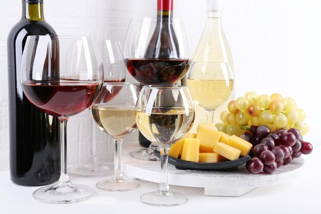 Photo bottles and glasses of wine cheese and ripe grapes on table in room
