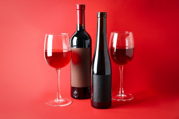 Bottles and glasses of wine on red background