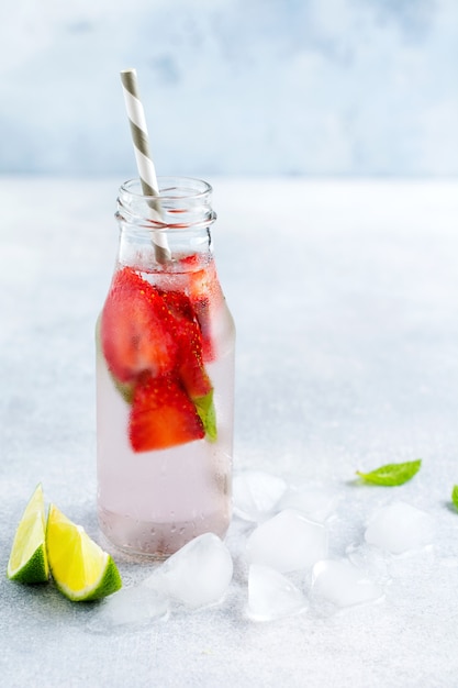 Bottles lemonade refreshing summer lemonade with lime, strawberry, cherry, cucumber and ice on a gray concrete surface. 