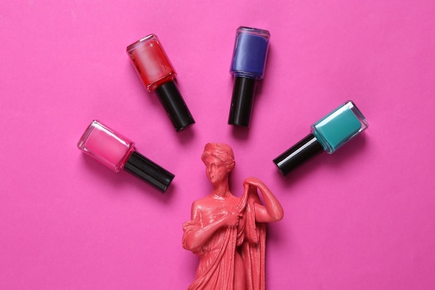 Bottles of nail polish and antique statue on pink background Beauty still life