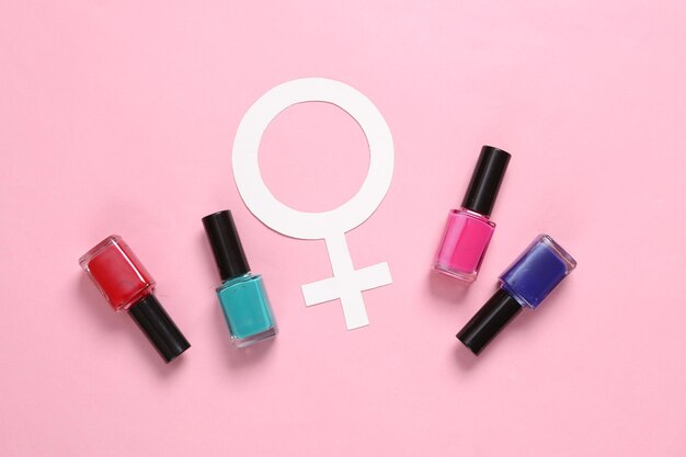 Bottles of nail polish and venus symbol on pink background Top view