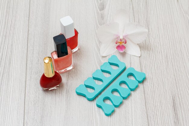 Bottles of nail polishes and toe separators on gray wooden background A set of cosmetic tools