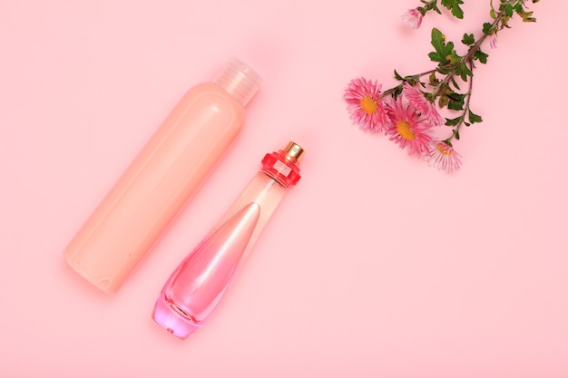 Bottiglie di profumo e shampoo su uno sfondo rosa con fiori. cosmetici e accessori donna. vista dall'alto.