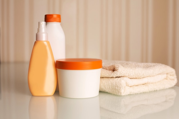 Bottles of shampoo, mask and hair lotion with bath towel on a desk over a neutral beige background. Space for text