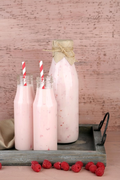 Бутылки вкусных малиновых смузи на розовом деревянном фоне