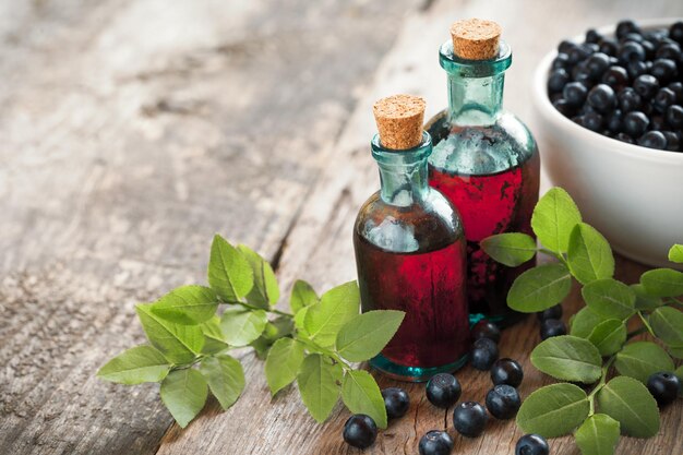 Bottles of tincture or cosmetic product and bowl with blueberries on wooden table