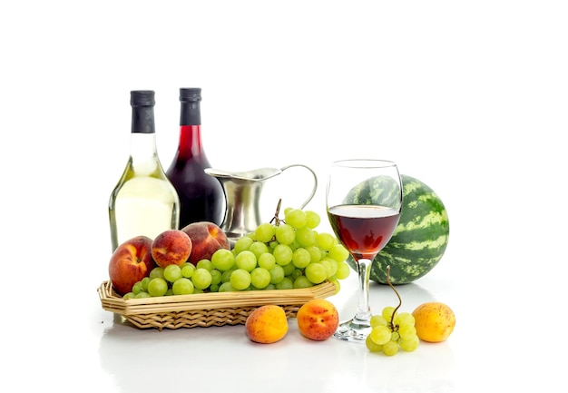 Bottles of wine pitcher glassful and ripe white grapes watermelon cherries peaches and apricots on a white background closeup