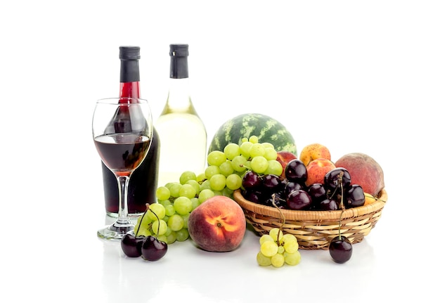 Bottles of wine pitcher glassful and ripe white grapes watermelon cherries peaches and apricots on a white background closeup