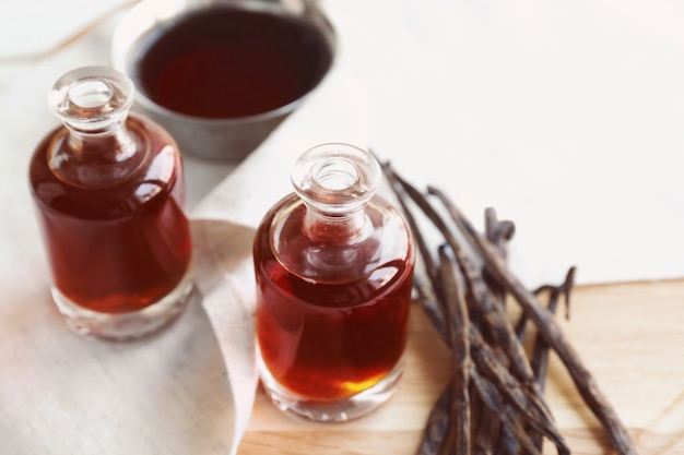 Bottles with aromatic extract and dry vanilla beans on table