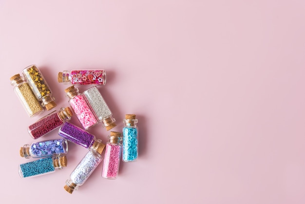 Bottles with bright glitters on pink background flat lay