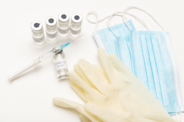 Bottles with coronavirus vaccine, developed for protection against COVID-19, healthcare syringe, medical mask and gloves