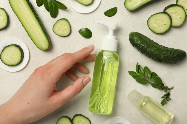 Bottles with cosmetics sliced cucumber and female hand on light background top view