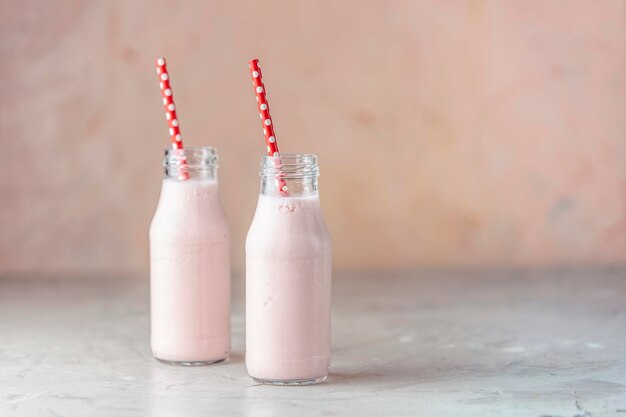 Photo bottles with delicious strawberry milkshake or smoothie on table and pink background