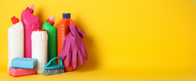 Bottles with detergent and cleaning supplies on yellow, space for text