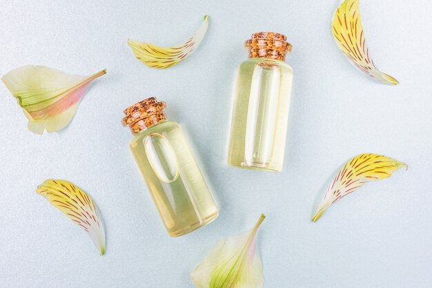 Bottles with floral essential oil and yellow flower petals on white