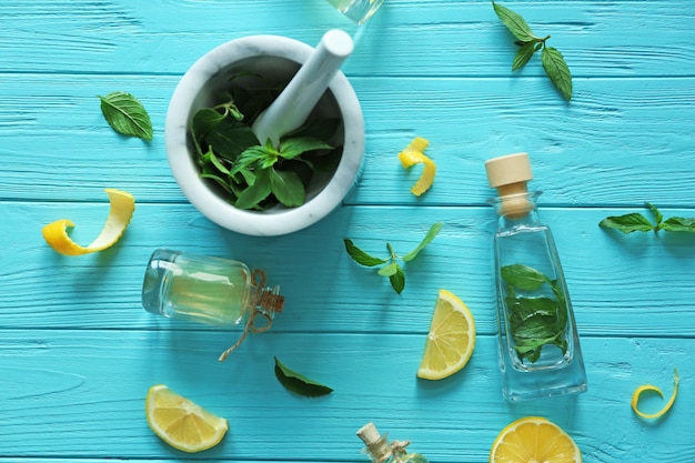 Bottles with mint oil and mortar with fresh leaves on wooden background top view