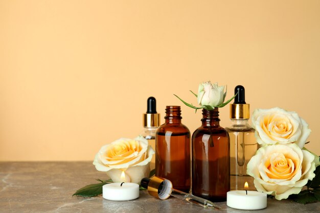 Bottles with rose essential oil, roses and candles against beige